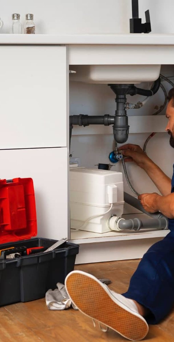 Plumber fixing pipes under kitchen sink